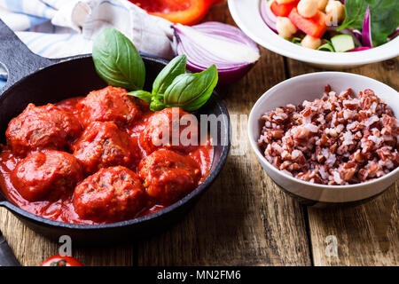 Fleischbällchen in gusseisernen Pfanne mit frischem Gemüse und Kichererbsen Salat und brauner Reis auf rustikalen Holztisch Stockfoto