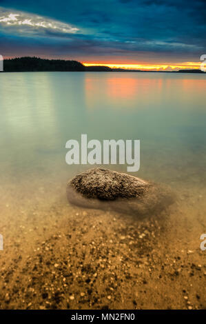 Panoramablick auf den See und mit dunklen Wolken am Himmel und Große glatte Steine in den vorderen während des Sonnenuntergangs. Stockfoto