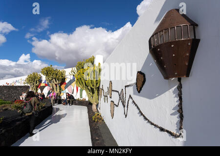 La Asomada, Lanzarote, Kanarische Inseln, Spanien: Touristische ruht in der Sonne gegen ein Mosaik Wand in den Garten der Fundacion Cesar Manrique Museum. Stockfoto