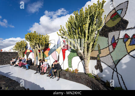 La Asomada, Lanzarote, Kanarische Inseln, Spanien: Touristische ruht in der Sonne gegen eine mozaiek Mauer im Garten der Fundacion Cesar Manrique Museum. Stockfoto