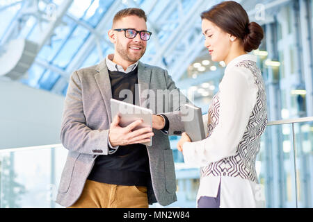 Taille bis Porträt der erfolgreiche junge Unternehmer im Gespräch mit weiblichen Kollegen stehen in der modernen Bürogebäude und glücklich lächelnd Stockfoto
