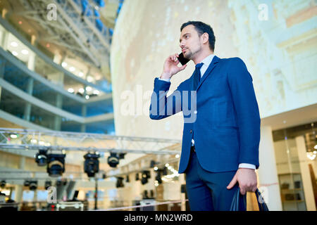 Seitenansicht Portrait von Stattlichen businesssman sprechen Telefonisch holding Gepäck in modernen Flughafen, Kopie Raum Stockfoto