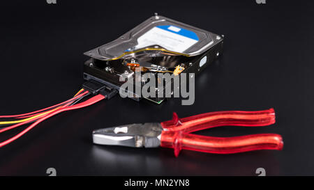 Festplatte und Zangen auf schwarzem Hintergrund. Open Storage Device mit geheimen Informationen. Schutz, Diebstahl oder Löschung von Daten, das Bipr, Bekämpfung der Cyberkriminalität. Stockfoto