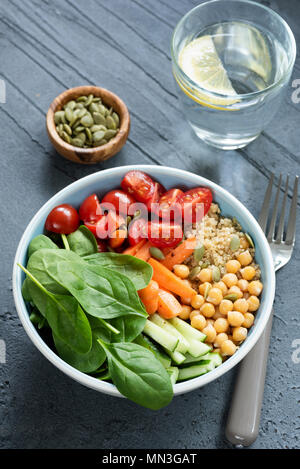 Kichererbsen salat Schüssel auf konkreten Hintergrund. Gesunde buddha Schüssel mit Baby, Spinat, Karotten, Kichererbsen, Quinoa und Tomaten/Paradeiser Stockfoto