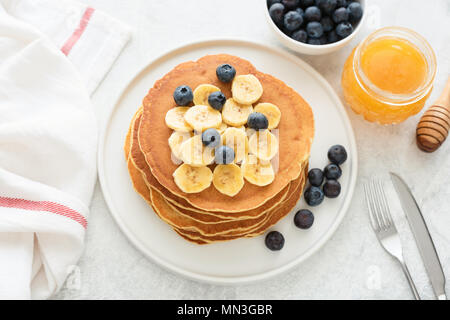 Hausgemachte Pfannkuchen mit Heidelbeeren und Banane auf weiße Platte. Stapel von Mais Pfannkuchen. Pfannkuchen mit Früchten und Honig auf einem Tisch Stockfoto