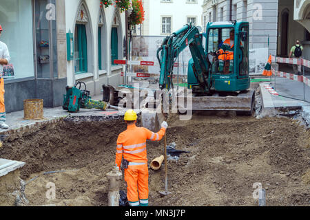 Luzern, Schweiz - Oktober 19, 2017: Arbeitnehmer in orange Uniformen Reparatur Kommunikation in der Altstadt und Baggern mit einem kleinen Bagger Stockfoto