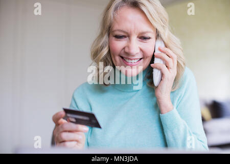 Lächelnd reife Frau mit Kreditkarte über Telefon Stockfoto
