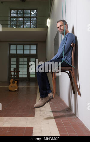 Mann sitzt auf einem Stuhl an der Kamera suchen, innen Stockfoto
