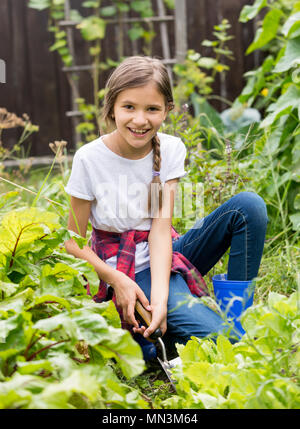 Porträt der Schönen lächelnden Teenager Sitzen im Garten und spudding Garden Bed Stockfoto