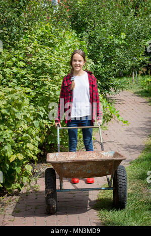 Lächelnd Jugendmädchen arbeiten im Garten und ziehen große Schubkarre Stockfoto