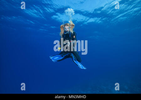 Weibliche Scuba Diver in der Lotus Position hing und wartet vergeht Dekompressionszeit auf Safety Stop im blauen Wasser Stockfoto