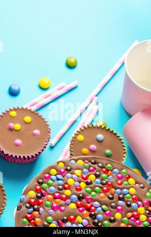 Milch Schokolade Kuchen mit mehrfarbig glasierten Candy besprüht Ranunkeln Papierbecher Rosa Strohhalme blauen Hintergrund. Party Feier Ki Stockfoto