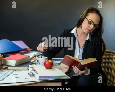 Foto von einem Lehrer oder Business Frau in den 30ern sitzen an einem Tisch vor einer großen Tafel zu lesen. Stockfoto