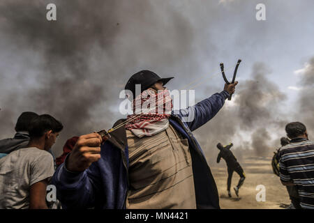 Khan Yunis, im südlichen Gazastreifen. 14 Mai, 2018. Eine palästinensische Demonstranten verwendet eine Schleuder Steine gegen israelische Sicherheitskräfte bei Auseinandersetzungen entlang der Israel-Gaza Grenze zu schleudern, auf der 70. Jahrestag der Nakba Tag (Tag der Katastrophe), die die Vertreibung vor und der Israelischen Unabhängigkeitserklärung von 1948 gefolgt, in Khan Yunis, im südlichen Gazastreifen, 14. Mai 2018. Credit: Mohammed Talatene/dpa/Alamy leben Nachrichten Stockfoto