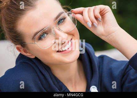 Schöne Mädchen oder Junge Frau mit perfekte Zähne entspannende außerhalb in einem blauen Hoody lachend Lächeln Brille Stockfoto