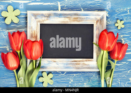 Blackboard und Haufen von roten Tulpen und Maiglöckchen Blumen auf blau im Hintergrund. Platz für Ihre test, Flach, straff Bild. Stockfoto