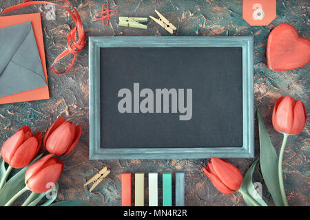 Frühling Urlaub Hintergrund: blackboard gerahmt mit roten Tulpen, Holz- Herzen, Farbe Kreide und Gruß Briefumschläge auf dunkel strukturierten Hintergrund, Platz für Stockfoto