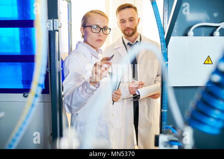 Bartgeier im mittleren Alter Inspektor und seiner schönen Kollegin tragen weiße Mäntel die notwendigen Notizen während der Durchführung von Qualitätskontrollen bei modernen Milch Stockfoto