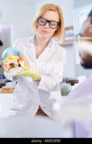 Portrait von weiblichen Zahnarzt holding Schädel Modell und erklären Zähne Regeln der Hygiene Patient im Behandlungsstuhl sitzen Stockfoto