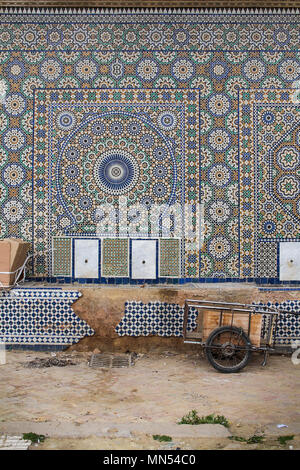 Wand mit einem traditionellen geometrischen Mosaik in Meknes, Marokko. Alte Karre im Vordergrund geparkt. Stockfoto