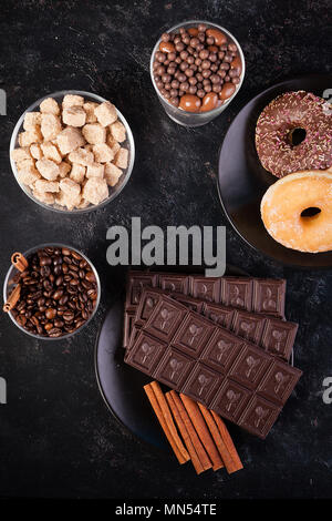 Blick von oben auf die Schokolade Tabletten, Donuts, brauner Zucker mit Erdnüssen in Schokolade und Kaffee Bohnen Stockfoto