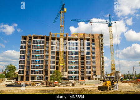 Baustelle mit zwei industriellen Turmdrehkrane am Bau der neuen Ziegel, hohes Gebäude mit einem gelben Traktor bulldozer am strahlend blauen Himmel, ein Stockfoto