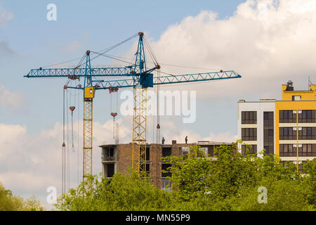 Stadtentwicklung Blick auf die Silhouetten von zwei hohen industriellen Turmdrehkrane am Bau neuer Ziegelgebäude mit Arbeitern in harte Hüte sie daran arbeiten und gegen BR Stockfoto