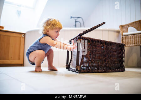 Kleinkind Junge spielt mit einem Wäschekorb im Bad. Stockfoto