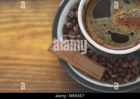 Braun Kaffee Tasse mit einem Schaum auf eine Untertasse mit Kaffeebohnen mit einem Stück Schokolade Stockfoto