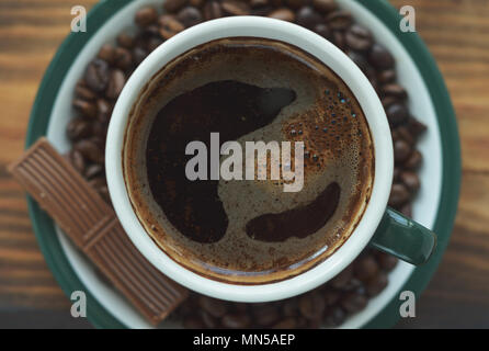 Grüne Tasse mit Kaffee auf eine Untertasse mit Kaffeebohnen und einem Stück Schokolade Stockfoto