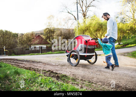 Ein Vater mit Kleinkind Sohn treibt ein Jogger außerhalb. Ein Spaziergang im Frühling Natur. Stockfoto