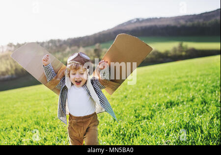 Glückliches Kind Junge mit Hut, Brille und Flügel spielen im Freien im Frühjahr die Natur. Pilot und fliegende Konzept. Stockfoto