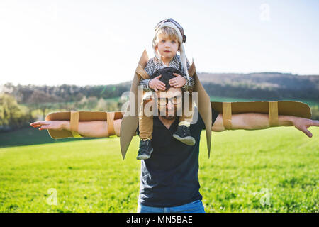 Glückliches Kind Junge mit Hut, Brille und Flügel spielen im Freien mit seinem Vater im Frühling Natur. Pilot und fliegende Konzept. Stockfoto