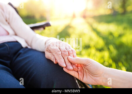 Nicht erkennbare Enkelin die Hand eines älteren Großmutter im Rollstuhl im Frühling Natur. Stockfoto