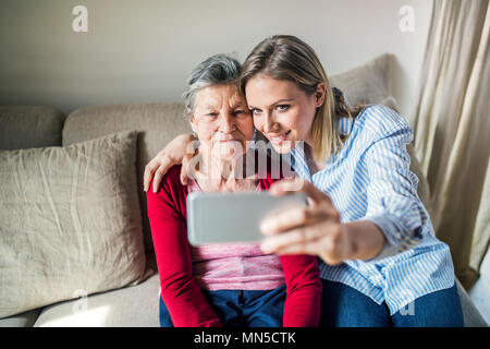 Eine alte Großmutter und Enkelin mit Smartphone zu Hause, sitzt auf einem Sofa und unter selfie. Stockfoto