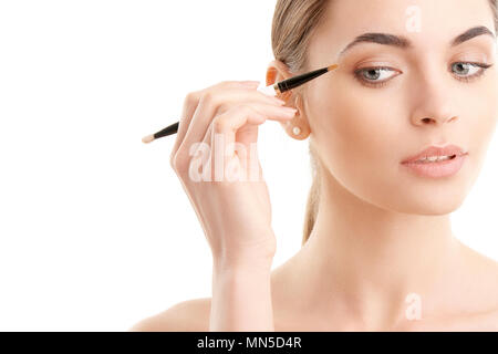 Studio geschossen von einer schönen jungen Frau Anwendung Make-up zu Ihrem Augenbraue beim Stehen an vereinzelten weißen Hintergrund mit kopieren. Stockfoto