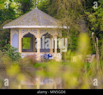 Celle, Niedersachsen, Deutschland, April 28, 2018: ein Paar auf einer Bank sitzen vor einem altmodischen kleinen Pavillon in einem öffentlichen Garten, INTENSIONALEN Stockfoto