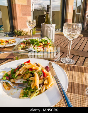 Tisch im Freien bei Sonnenschein mit Pasta Salat Teller serviert auf einem weissen Teller, crystal Weingläser und eine Flasche kühlen Weißwein im Kühler Stockfoto