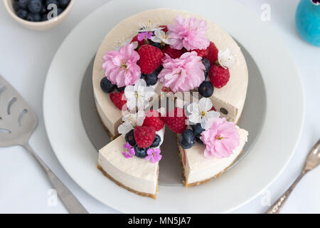 Ein Stück hausgemachten Veganer Käsekuchen zum Dessert. Mit Himbeeren, Heidelbeeren und frische Frühling Blüten dekoriert. Stockfoto