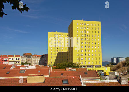 Leuchtend gelbe Wohnblocks, hoch über dem orange Kacheln auf die Dächer der normale Häuser an einem sonnigen Tag mit blauen Himmel. In den Vororten von Lisb gefunden Stockfoto