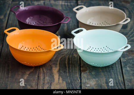 Bunte Kunststoff colanders mit Griffen auf Blau Holz- Hintergrund Stockfoto