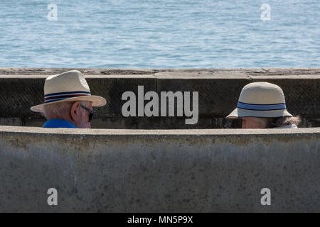 Zwei ältere Menschen, Mann und Frau zurückgezogen und sitzen auf einer Bank am Meer tragen traditionell britischen Panama Hüte vor der Sonne zu schützen. Stockfoto