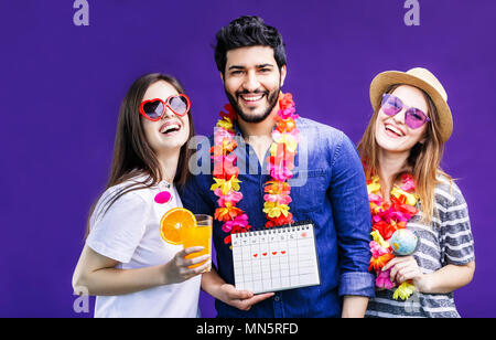 Glücklich lächelnde Freunde, zwei Mädchen und bärtiger Mann, hält Ferienhäuser reise Kalender vor dem violetten Hintergrund Stockfoto