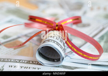 Rollen von Geld in einem geschenkband auf Rechnungen von Dollar und Euro Stockfoto