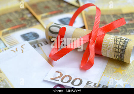 Rollen von Geld in einem geschenkband auf Rechnungen von Dollar und Euro Stockfoto