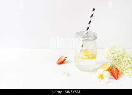 Styled Foto. Noch immer leben Zusammensetzung mit hausgemachten elderflowers Limonade in Glas trinken jar, Zitronen, Erdbeeren und wilde Rosen auf Weiß Holztisch. Sommer Garden Party Hintergrund. Stockfoto