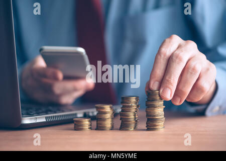 Geschäftsmann mit Smartphone mit gestapelten Münzen im Vordergrund, in der Nähe geschossen mit selektiven Fokus Stockfoto