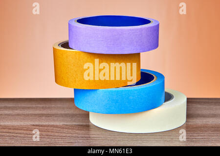 Vier mehrfarbige Klebeband oder Klebebänder sind übereinander gestapelt auf dem Tisch, auf orangem Hintergrund. Stockfoto