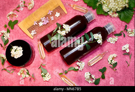 Durchstechflaschen mit Haarpflege Produkt in frische Blumen auf einem rosa Handtuch. Stockfoto