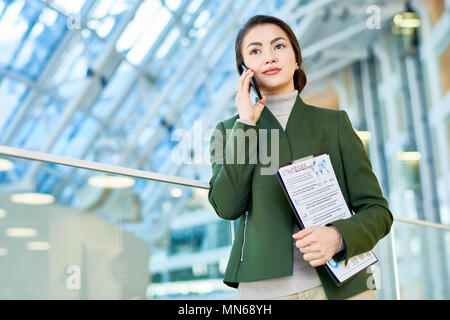Taille bis Portrait von erfolgreichen Asiatischen business lady Sprechen per Telefon stehen auf Glas Balkon in modernen Büro Gebäude, Raum Stockfoto